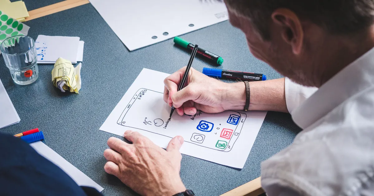 A designer sketches mobile app screens on paper with colored markers